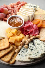 Photo of Different types of cut cheese and other snacks on grey textured table, closeup