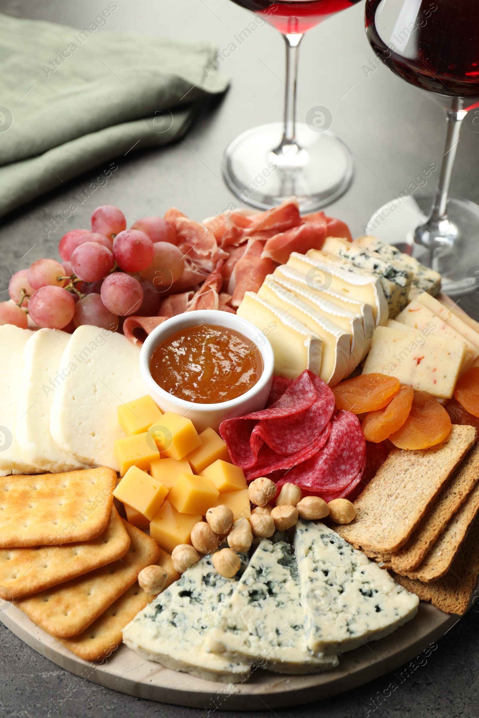 Photo of Different types of cut cheese and other snacks on grey textured table, closeup