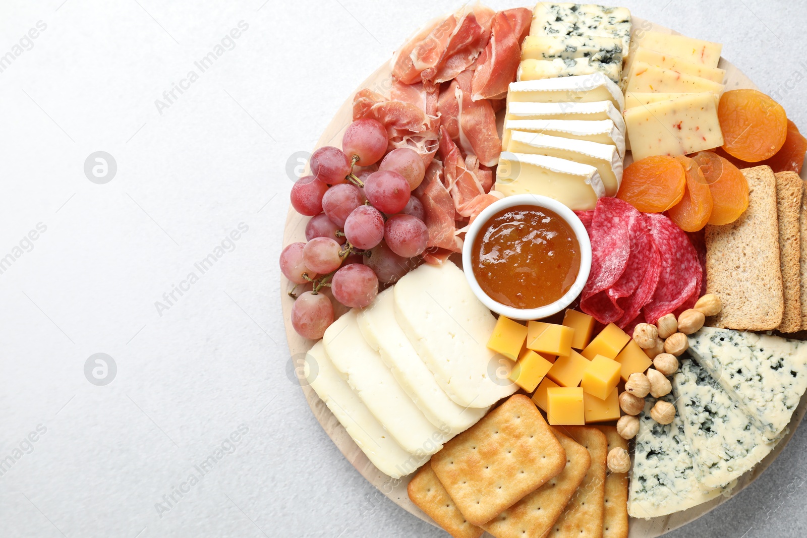 Photo of Different types of cut cheese and other snacks on light textured table, top view. Space for text