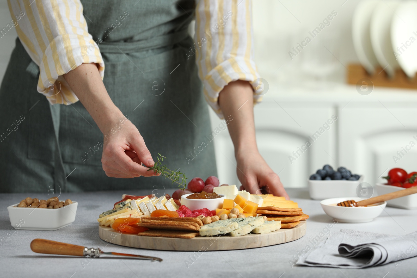 Photo of Woman serving antipasto platter with different types of cheese and other snacks with thyme at grey textured table indoors, closeup