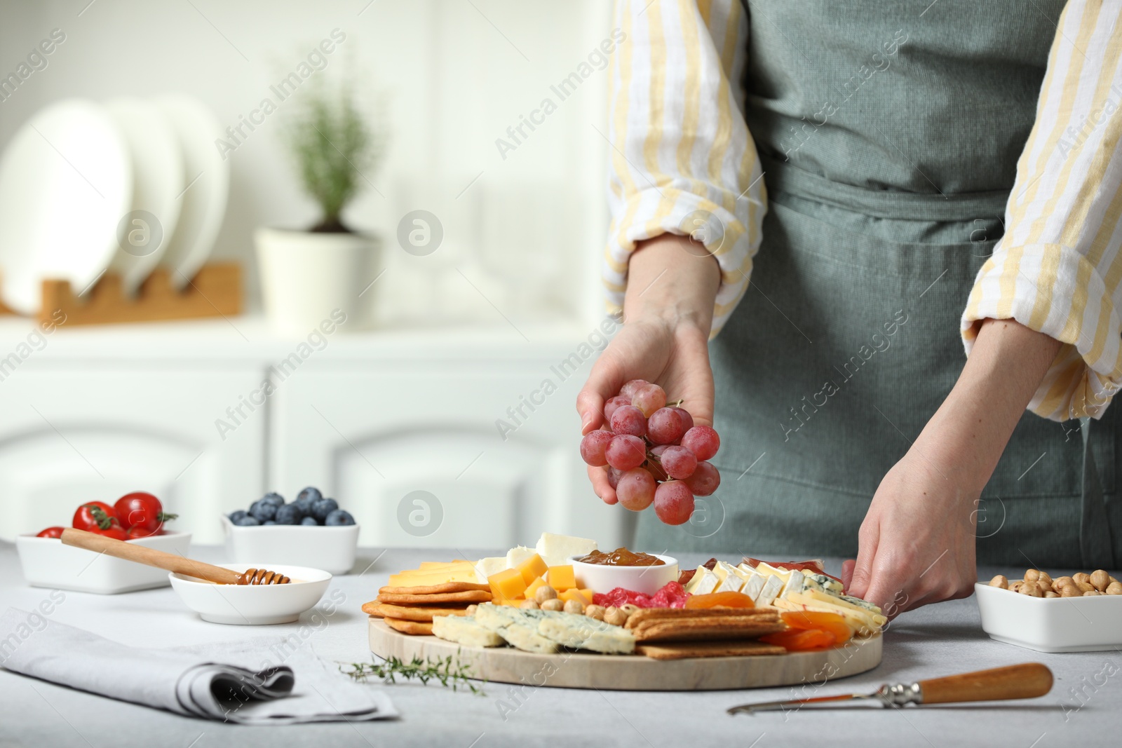 Photo of Woman serving antipasto platter with different types of cheese and other snacks with grapes at grey textured table indoors, closeup