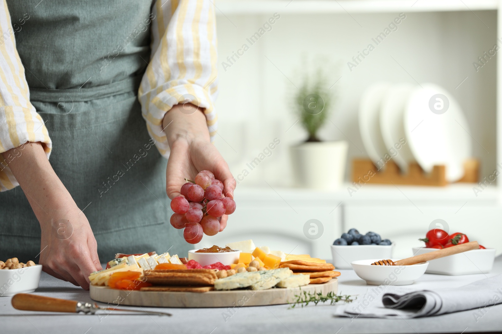 Photo of Woman serving antipasto platter with different types of cheese and other snacks with grapes at grey textured table indoors, closeup. Space for text