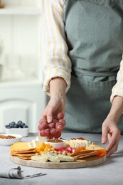 Photo of Woman serving antipasto platter with different types of cheese and other snacks with grapes at grey textured table indoors, closeup