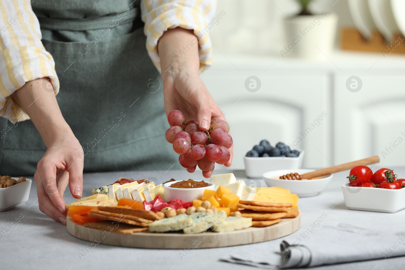 Photo of Woman serving antipasto platter with different types of cheese and other snacks with grapes at grey textured table indoors, closeup