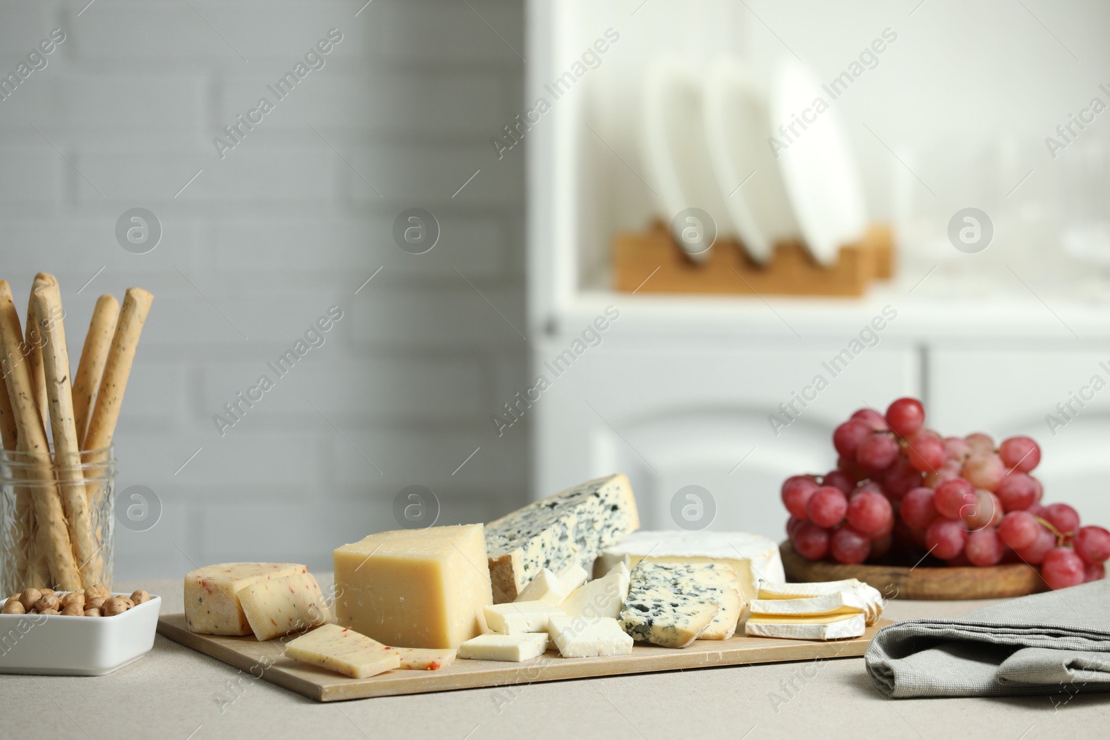 Photo of Different types of cut cheese and other snacks on light textured table indoors