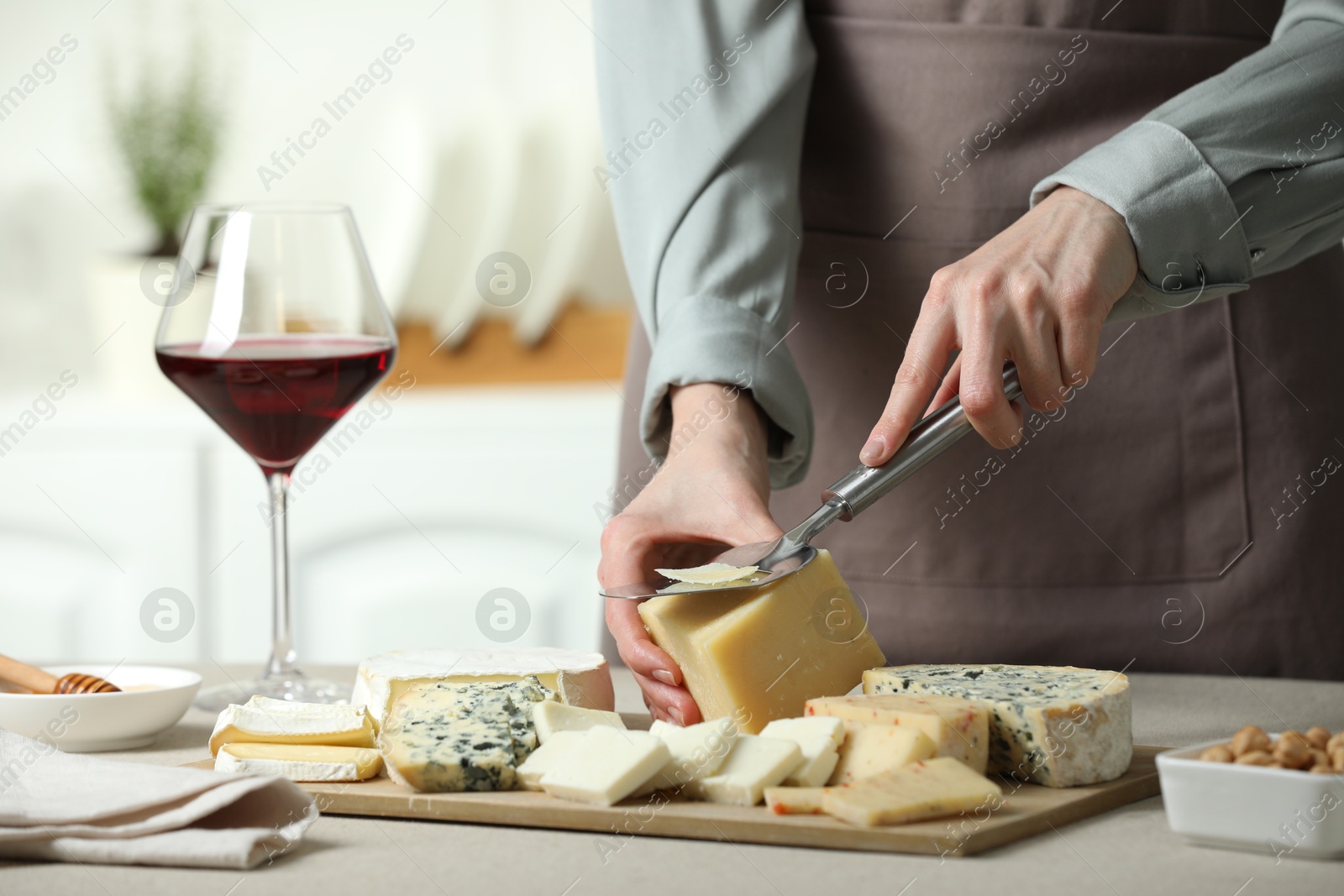 Photo of Woman slicing delicious cheese at light textured table indoors, closeup