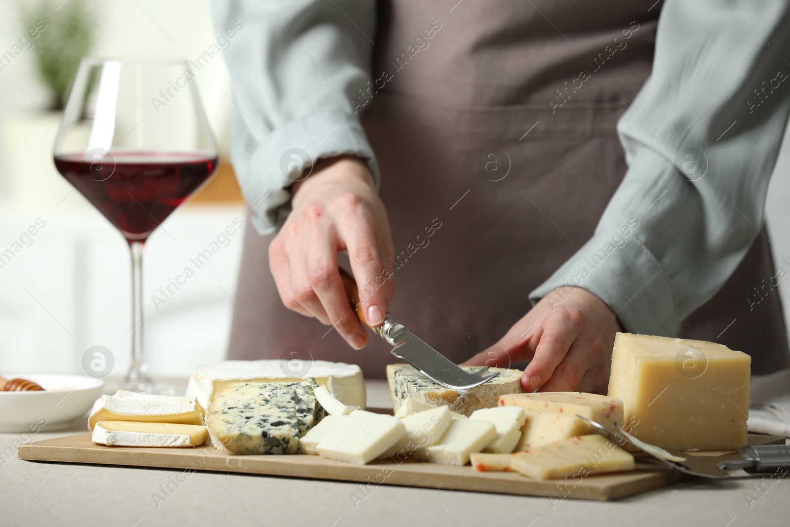 Photo of Woman slicing delicious cheese at light textured table indoors, closeup