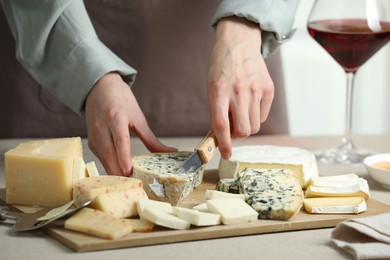 Photo of Woman slicing delicious cheese at light textured table indoors, closeup