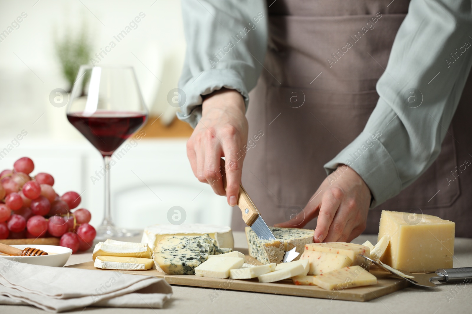 Photo of Woman slicing delicious cheese at light textured table indoors, closeup