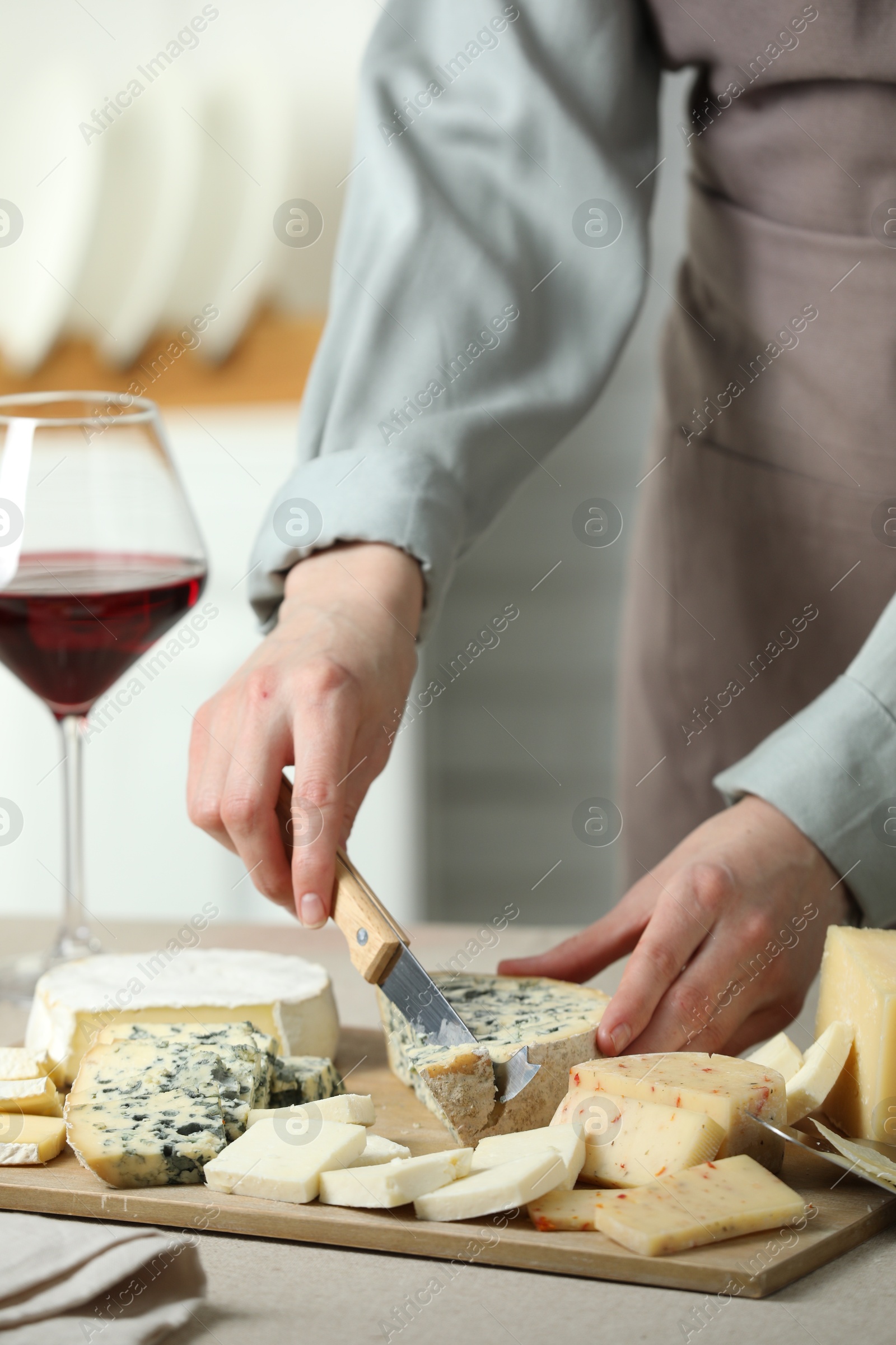 Photo of Woman slicing delicious cheese at light textured table indoors, closeup