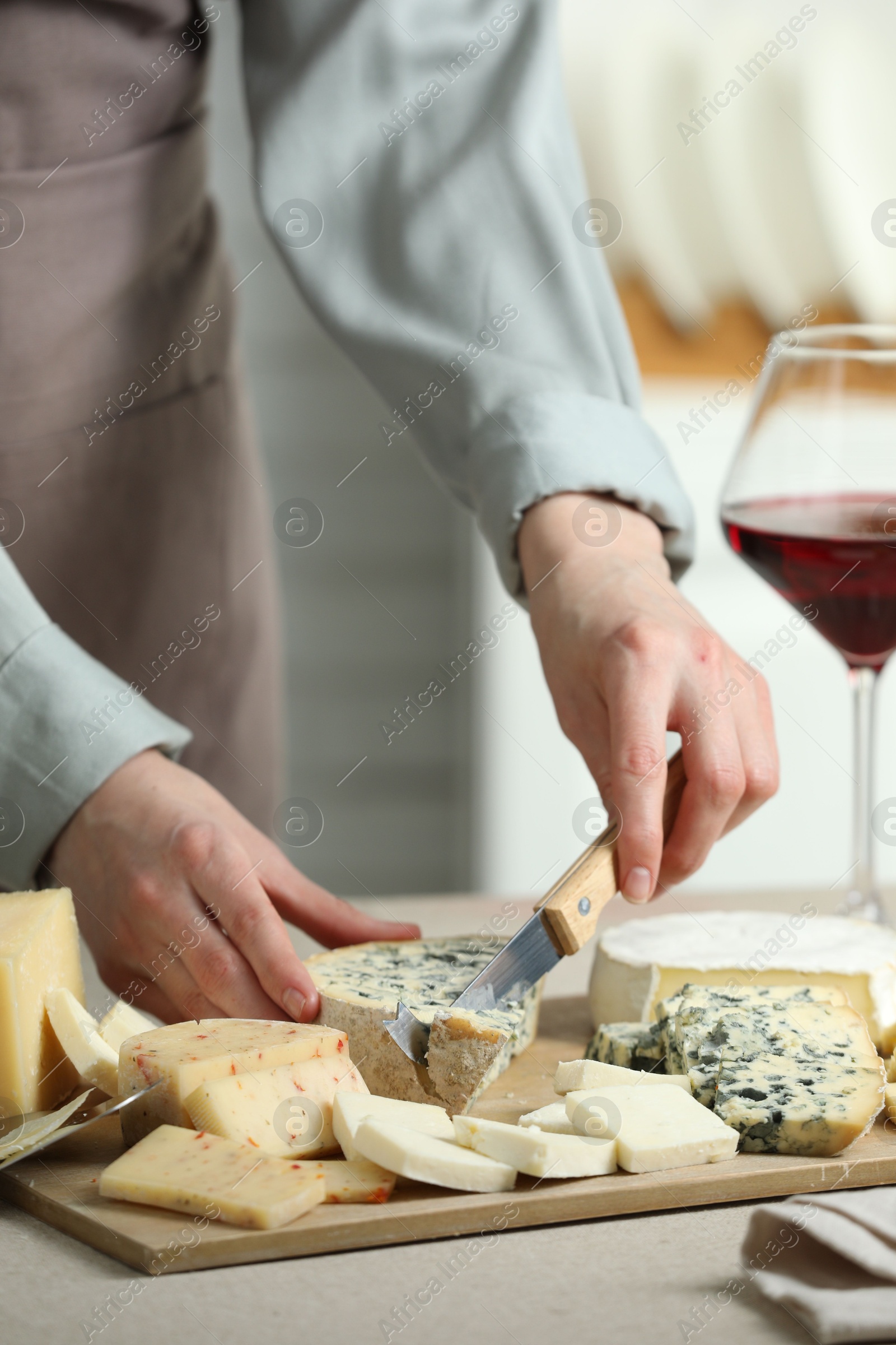 Photo of Woman slicing delicious cheese at light textured table indoors, closeup