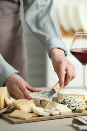 Photo of Woman slicing delicious cheese at light textured table indoors, closeup