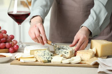 Photo of Woman slicing delicious cheese at light textured table indoors, closeup