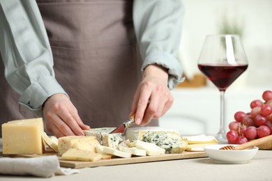 Photo of Woman slicing delicious cheese at light textured table indoors, closeup