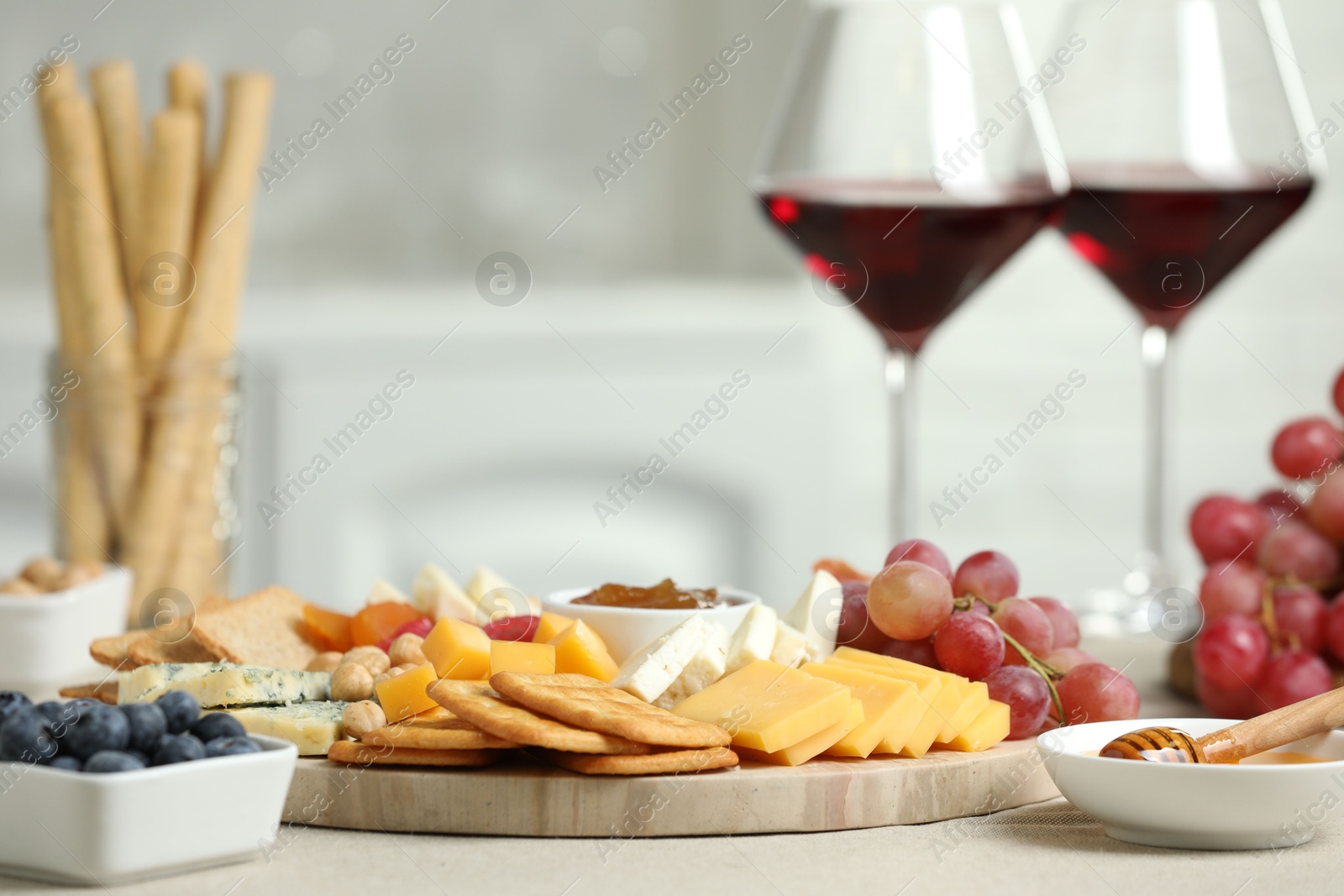 Photo of Different types of cut cheese and other snacks on light textured table, closeup