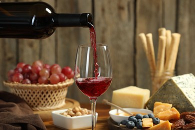 Photo of Pouring red wine into glass at table with different snacks, closeup