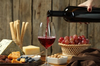 Photo of Woman pouring red wine into glass at table with different snacks, closeup