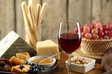 Photo of Red wine and different snacks served on wooden table, closeup