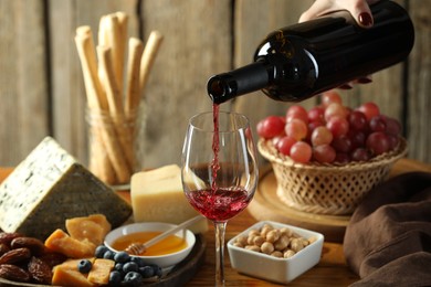 Photo of Woman pouring red wine into glass at table with different snacks, closeup