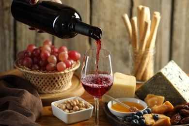 Photo of Woman pouring red wine into glass at table with different snacks, closeup