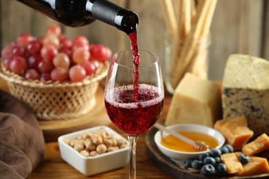 Photo of Pouring red wine into glass at table with different snacks, closeup