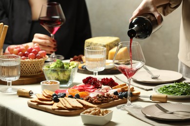 Photo of Woman pouring wine into glass at table with different snacks indoors, closeup