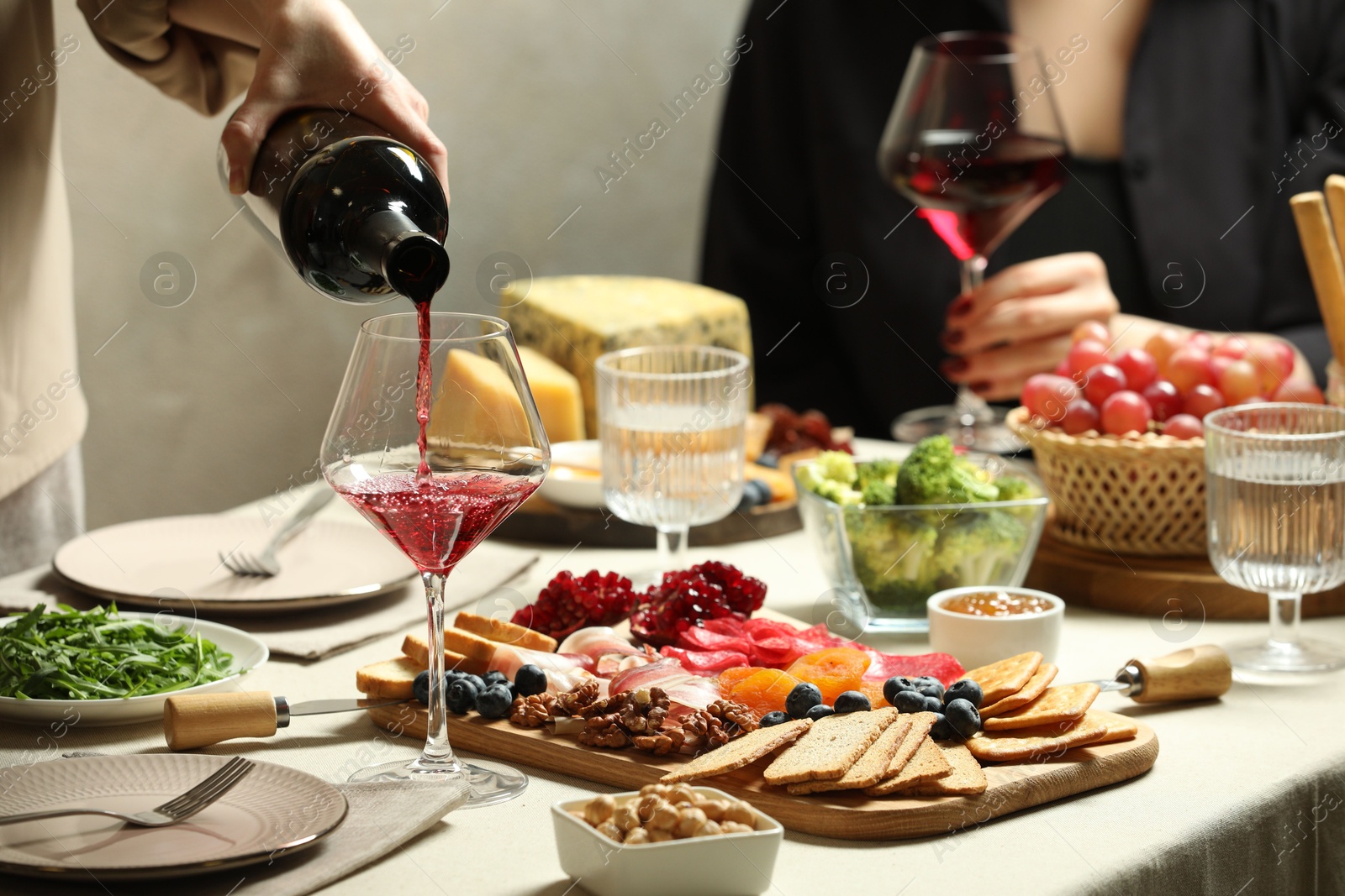 Photo of Woman pouring wine into glass at table with different snacks indoors, closeup