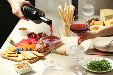 Photo of Woman pouring wine into glass at table with different snacks indoors, closeup