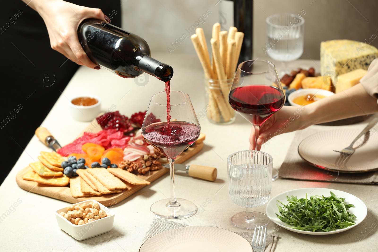 Photo of Woman pouring wine into glass at table with different snacks indoors, closeup