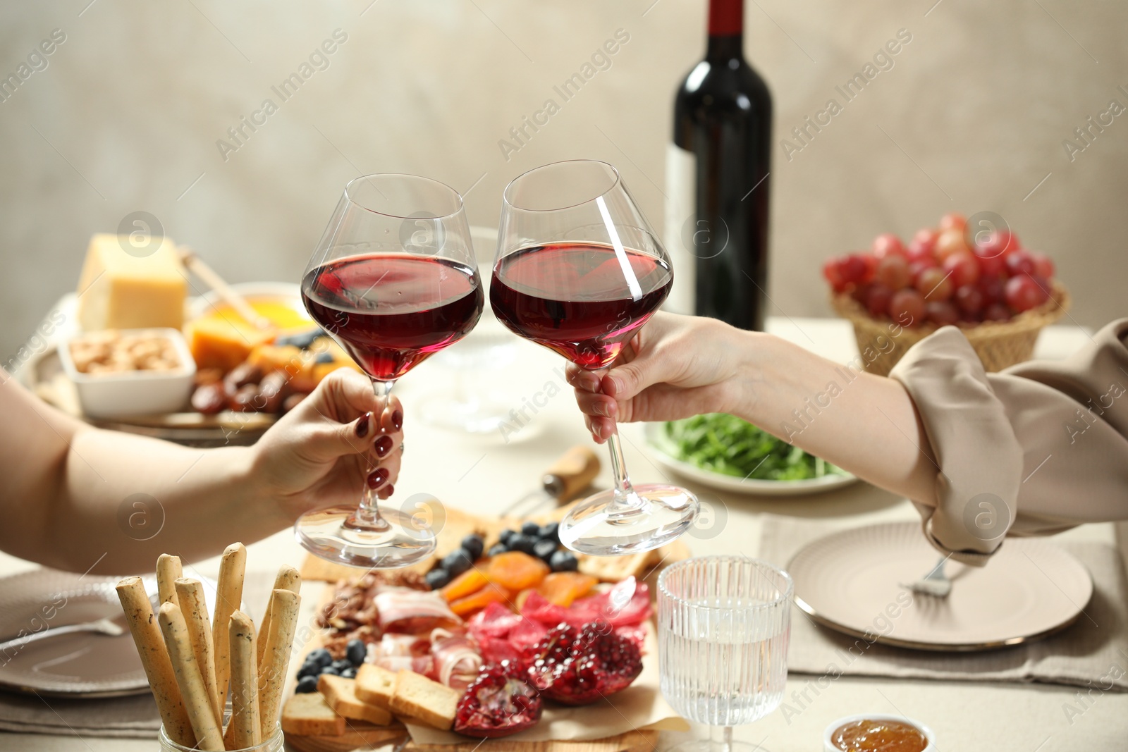 Photo of Women clinking glasses of wine during dinner at table indoors, closeup