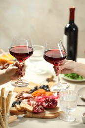 Photo of Women clinking glasses of wine during dinner at table indoors, closeup