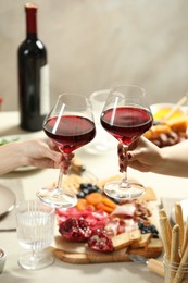 Photo of Women clinking glasses of wine during dinner at table indoors, closeup