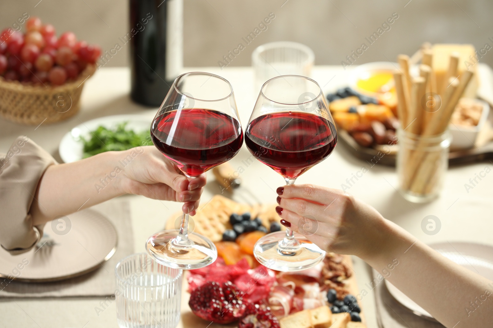 Photo of Women clinking glasses of wine during dinner at table indoors, closeup