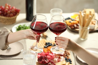 Photo of Women clinking glasses of wine during dinner at table indoors, closeup