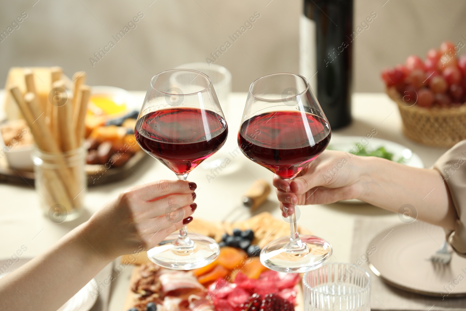 Photo of Women clinking glasses of wine during dinner at table indoors, closeup