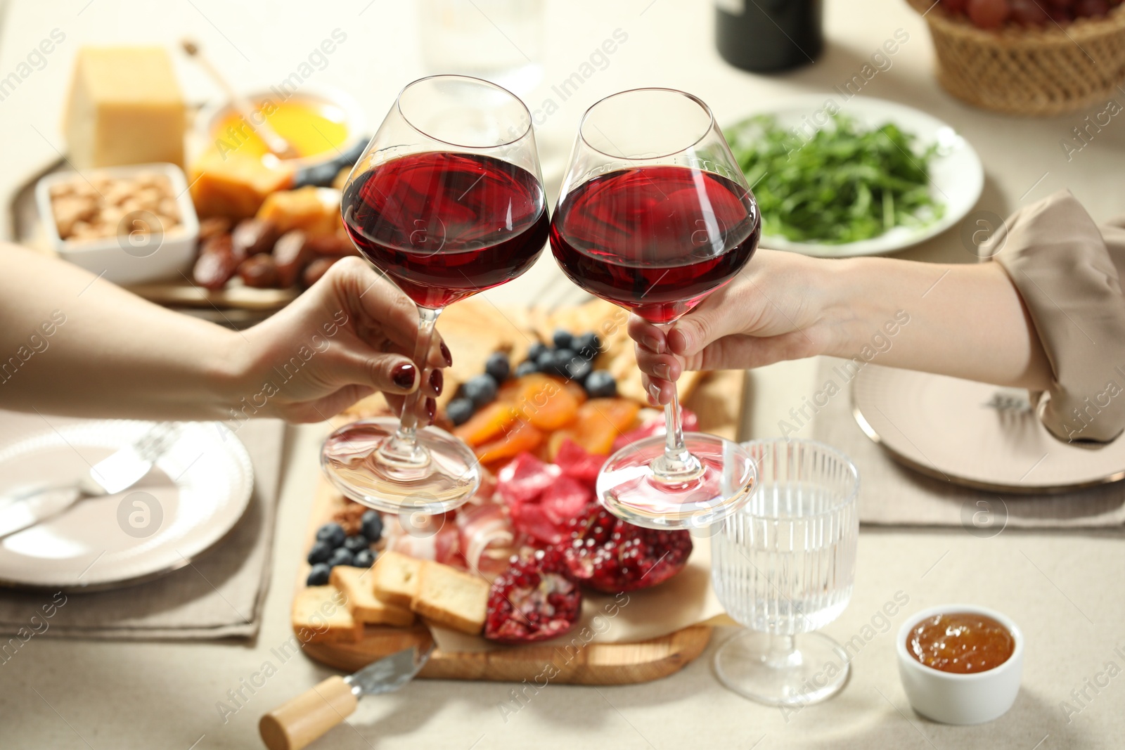 Photo of Women clinking glasses of wine during dinner at table indoors, closeup