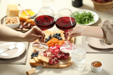 Photo of Women clinking glasses of wine during dinner at table indoors, closeup