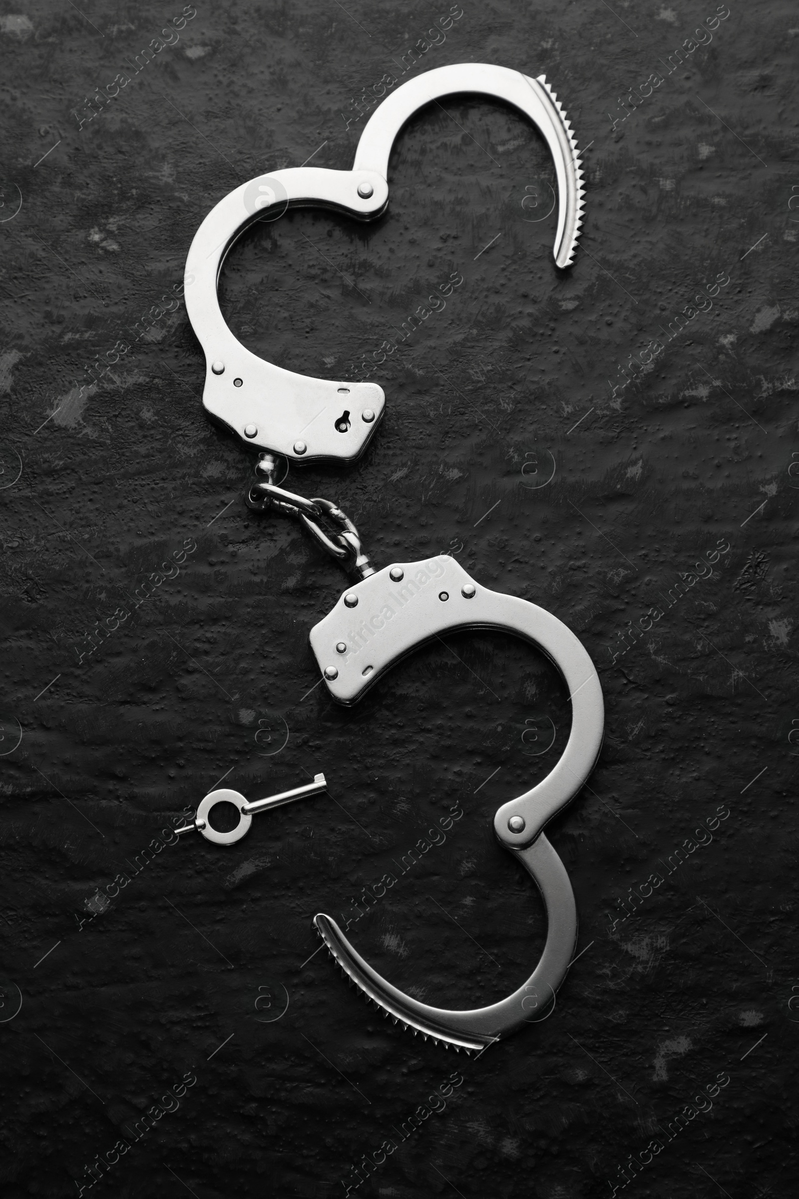 Photo of Metal chain handcuffs and key on black table, top view