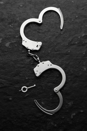 Photo of Metal chain handcuffs and key on black table, top view