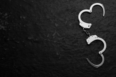 Photo of Metal chain handcuffs on black table, top view. Space for text