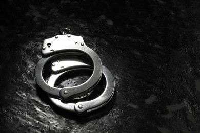 Photo of Metal chain handcuffs on black table, closeup. Space for text