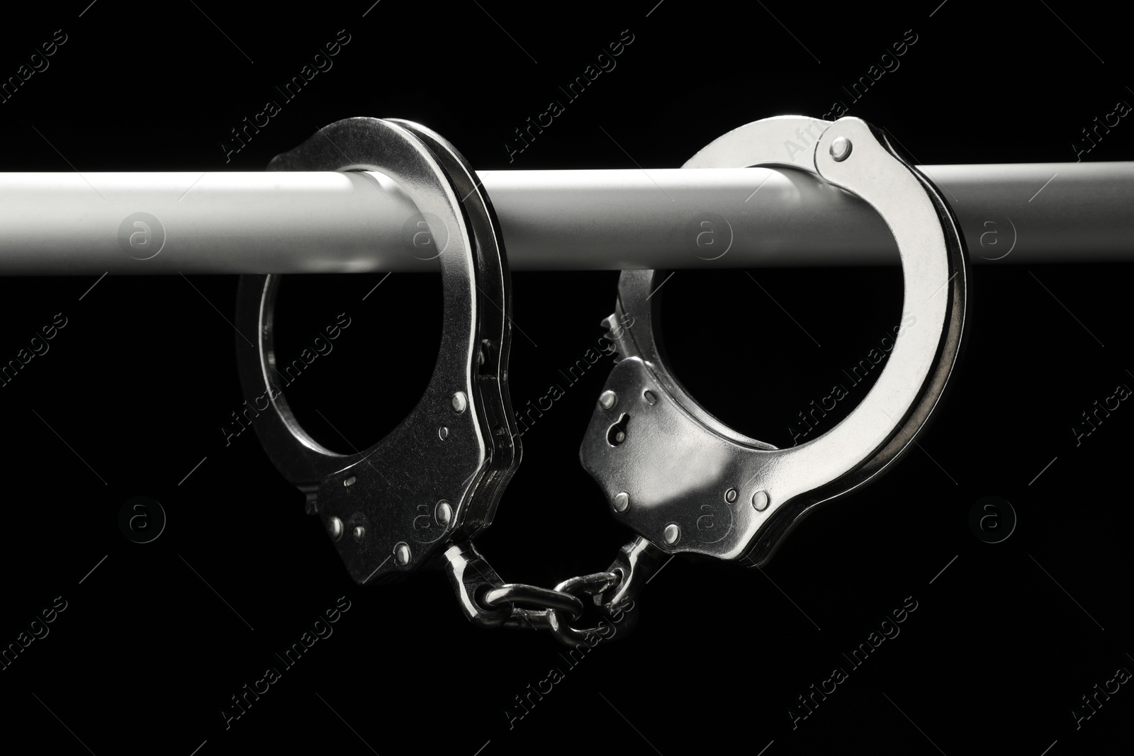 Photo of Metal chain handcuffs on pipe against black background, closeup