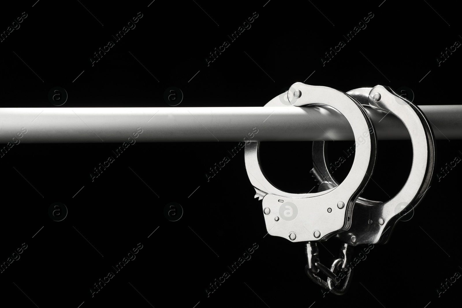 Photo of Metal chain handcuffs on pipe against black background, closeup