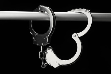 Photo of Metal chain handcuffs on pipe against black background, closeup