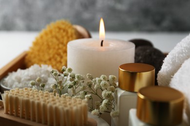 Photo of Burning candle and other spa supplies on table, closeup