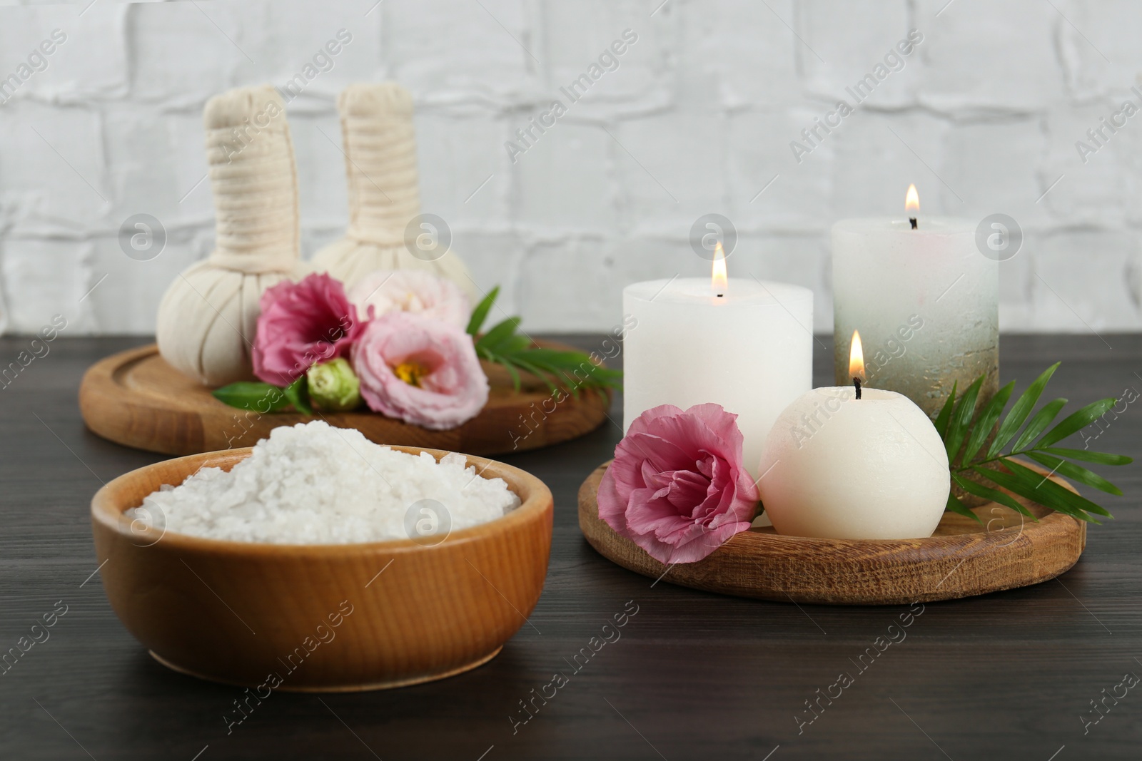 Photo of Spa treatment. Massage bags, sea salt, burning candles and flowers on wooden table