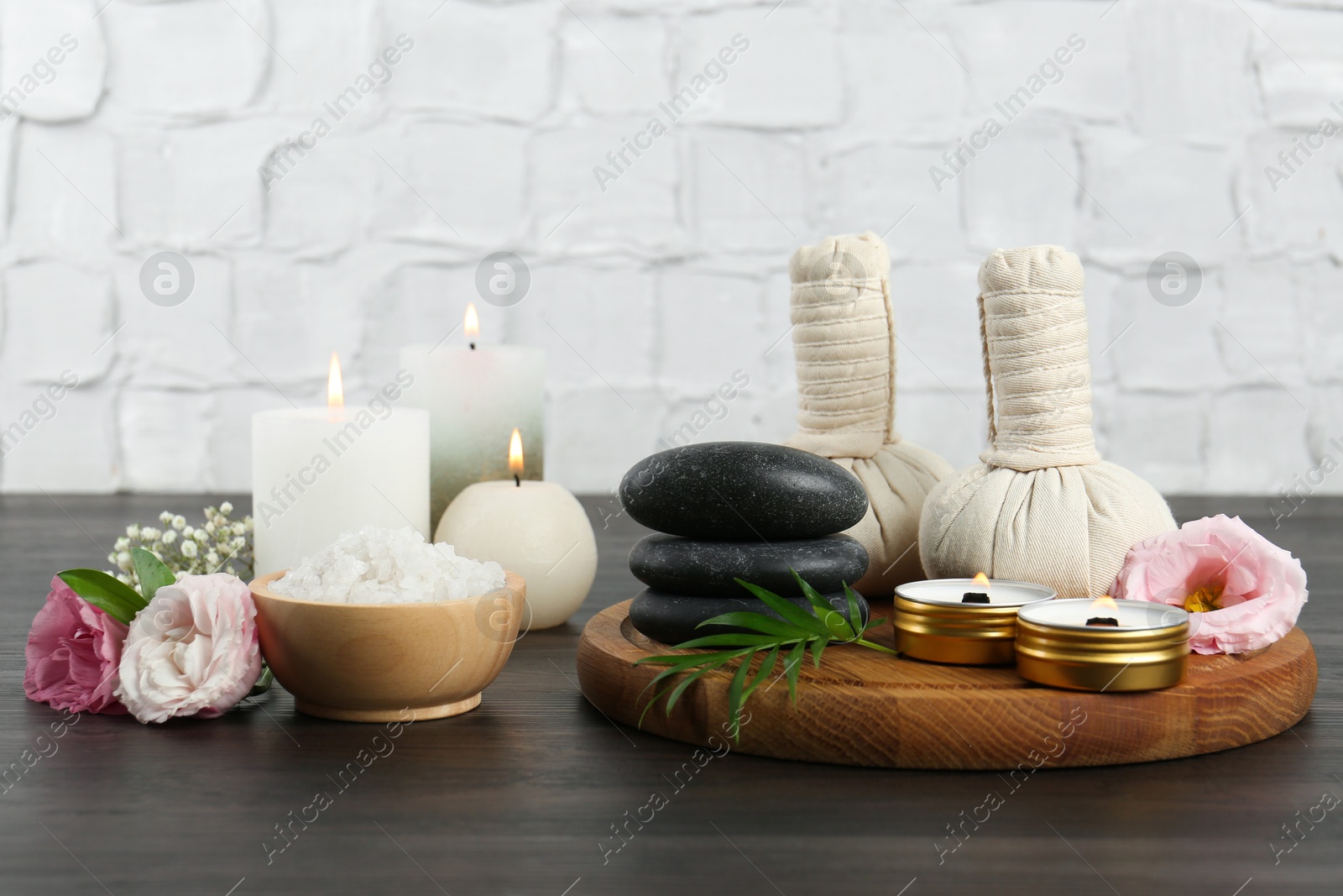 Photo of Massage bags, spa stones, sea salt, burning candles and flowers on wooden table