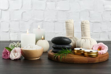 Photo of Massage bags, spa stones, sea salt, burning candles and flowers on wooden table