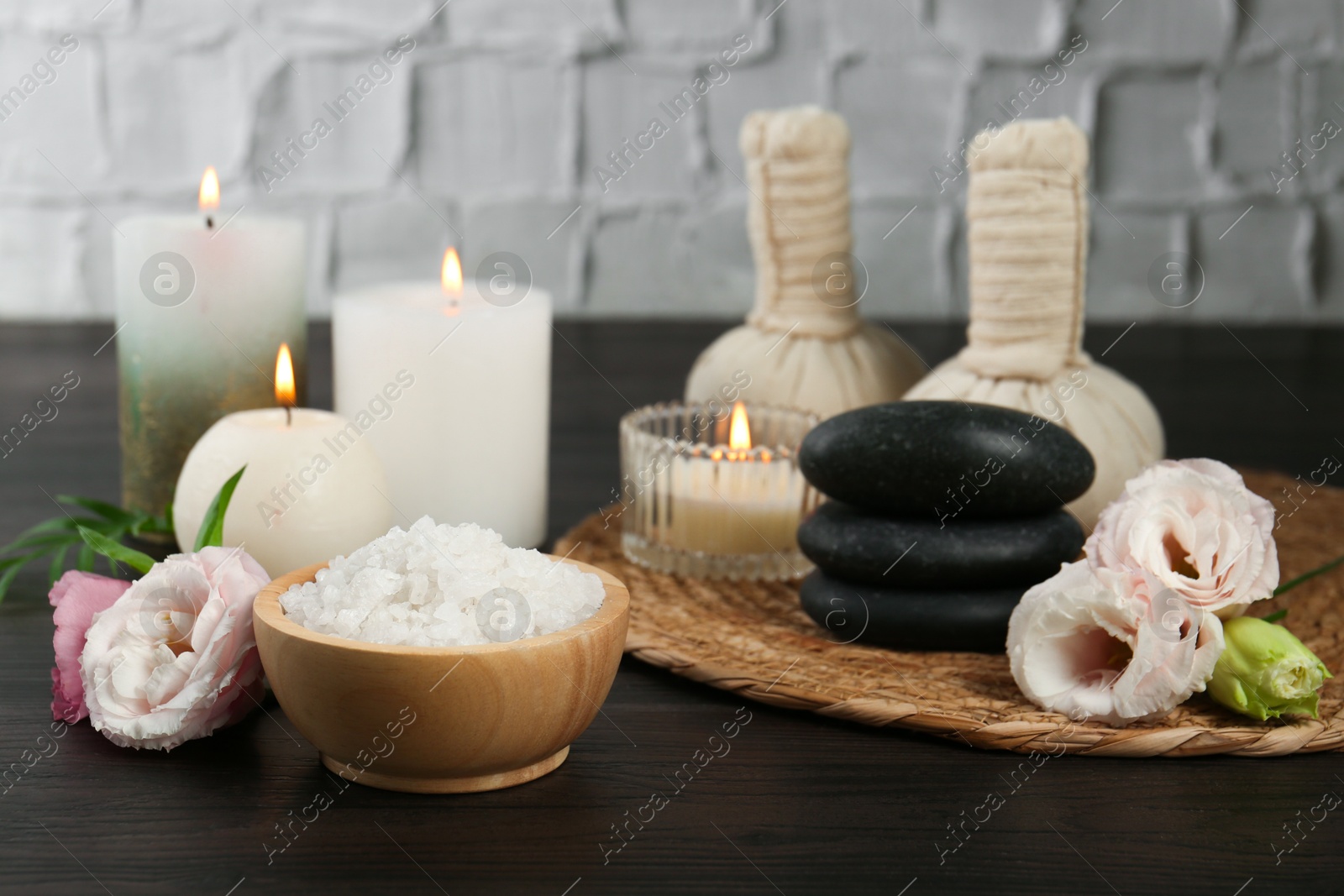 Photo of Massage bags, spa stones, sea salt, burning candles and flowers on wooden table