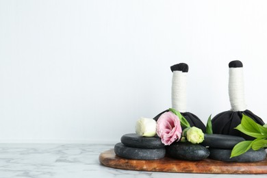 Photo of Massage bags, spa stones and beautiful flowers on white marble table. Space for text